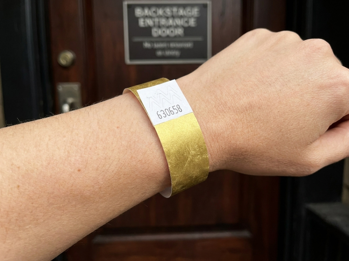 VIP-festivaaliranneke kultaisella metallipainatuksella ja viivakoodilla, käytettynä ranteessa backstage-sisäänkäynnin edessä