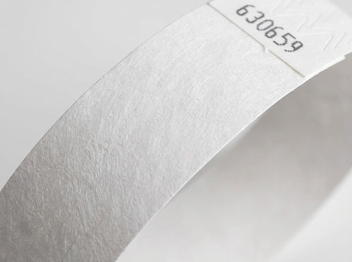 Lähikuva valkoisen Tyvek-rannekkeen kuitumateriaalin pinnasta, joka näyttää korkeatiheyspolyeteenin tunnusomaisen tekstuurin